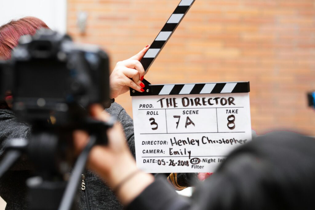 pexels-photo-1117132-1117132 Close-up of film clapperboard in action with camera filming a take on set.